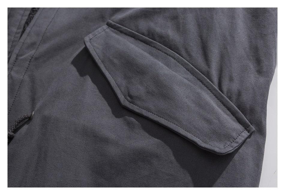 Close-up of a charcoal jacket sleeve pocket with a pointed flap and visible stitching.