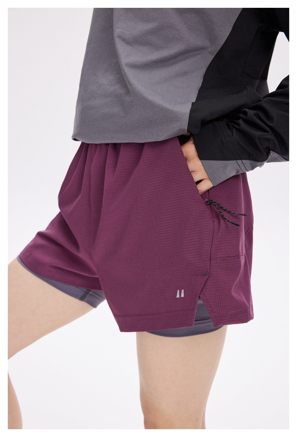 Close view of a model wearing plum running shorts over gray compression shorts, with a side pocket and drawcord.