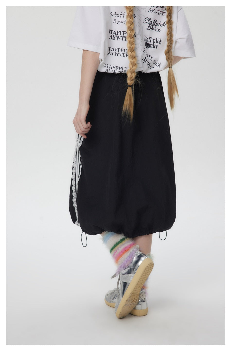 Back view of a model wearing a black gathered midi skirt with white lace side trim and a cinched hem.