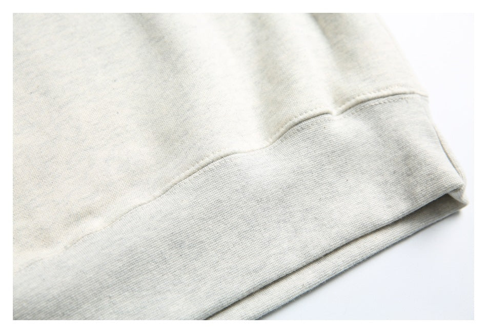 Close-up of a light heathered sweatshirt hem with a wide ribbed band and visible stitching.
