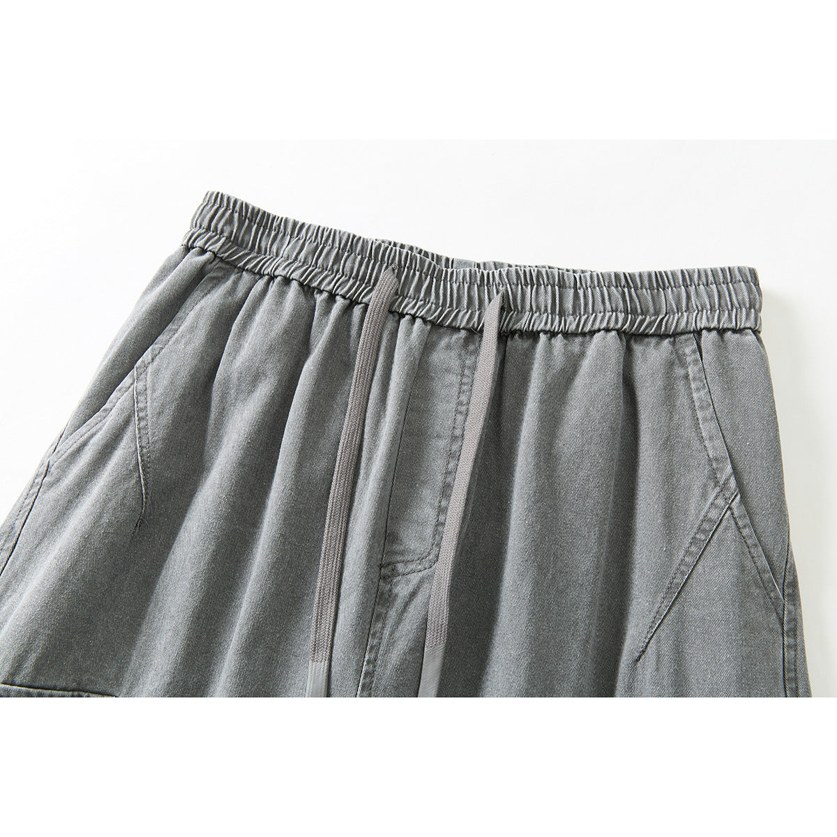 Close-up of gray cargo pants showing an elastic waistband, long drawstrings, and angled front pockets.