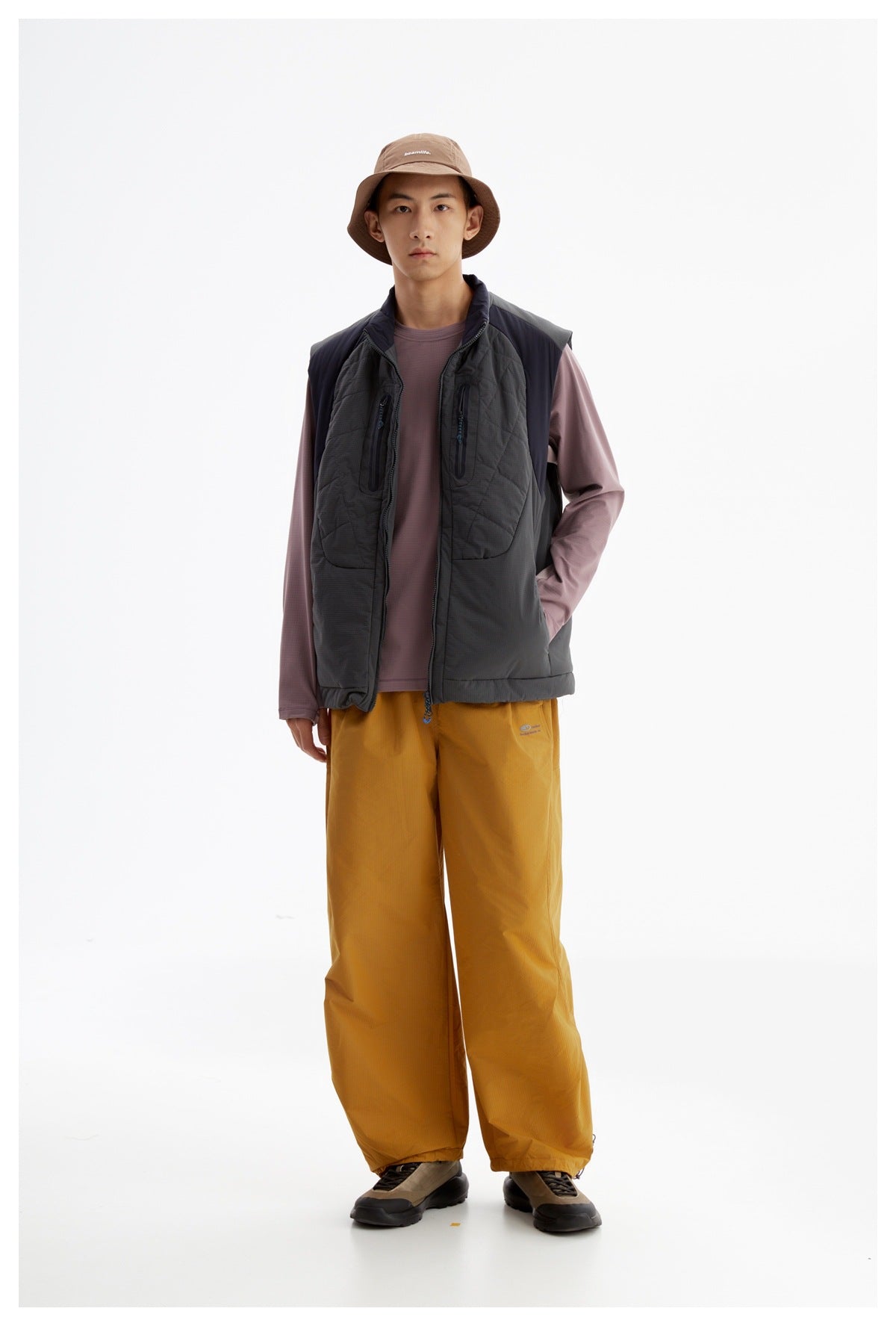 Front view of a model wearing a charcoal quilted utility vest with a mauve shirt and mustard wide-leg pants.