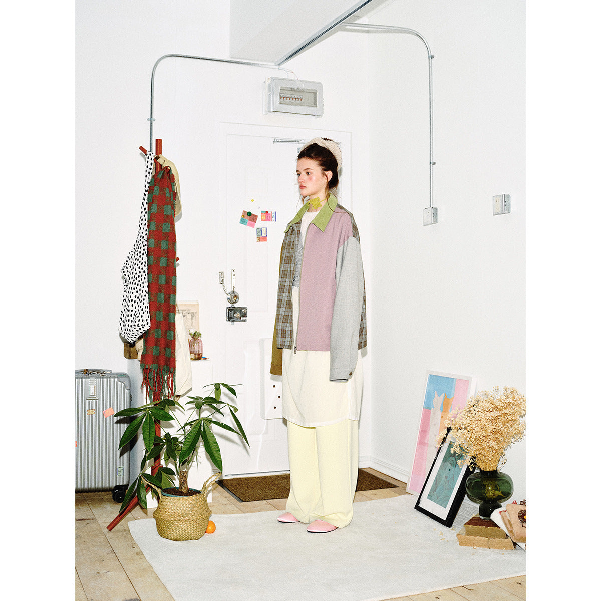 Full-length side view of a model wearing a multicolor patchwork jacket with a green collar and plaid panel.