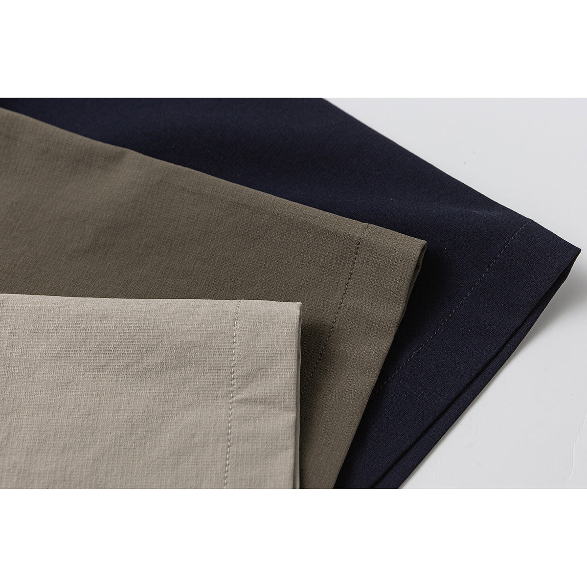 Close-up of overlapping light beige, olive, and navy fabric sections with stitched hems.