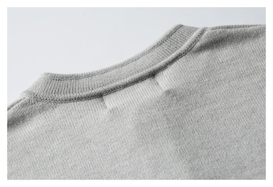 Close-up of the ribbed crew neckline and knit texture of a light gray sweater.
