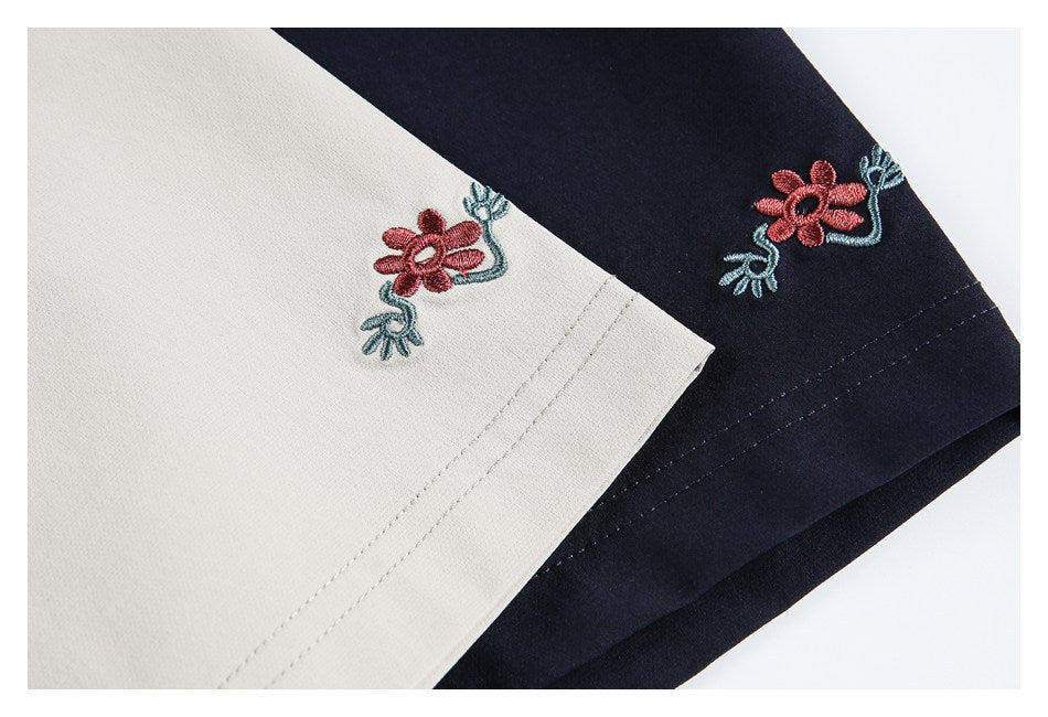 Close-up of matching pink and teal flower embroidery on cream and navy garment fabric.