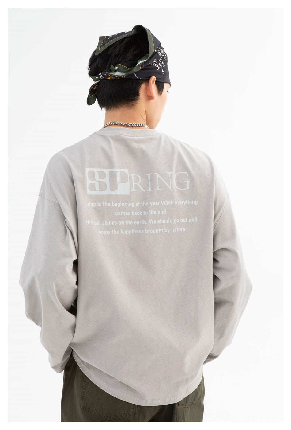 Person viewed from behind wearing a light gray oversized long-sleeve shirt with a white SPRING graphic on the back.