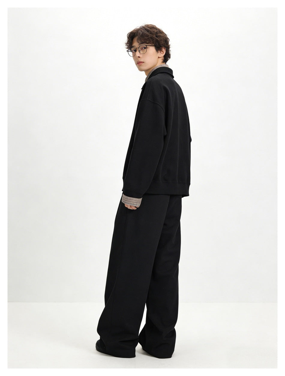 Rear three-quarter view of a model wearing a black pullover with plaid collar detail and loose black trousers.
