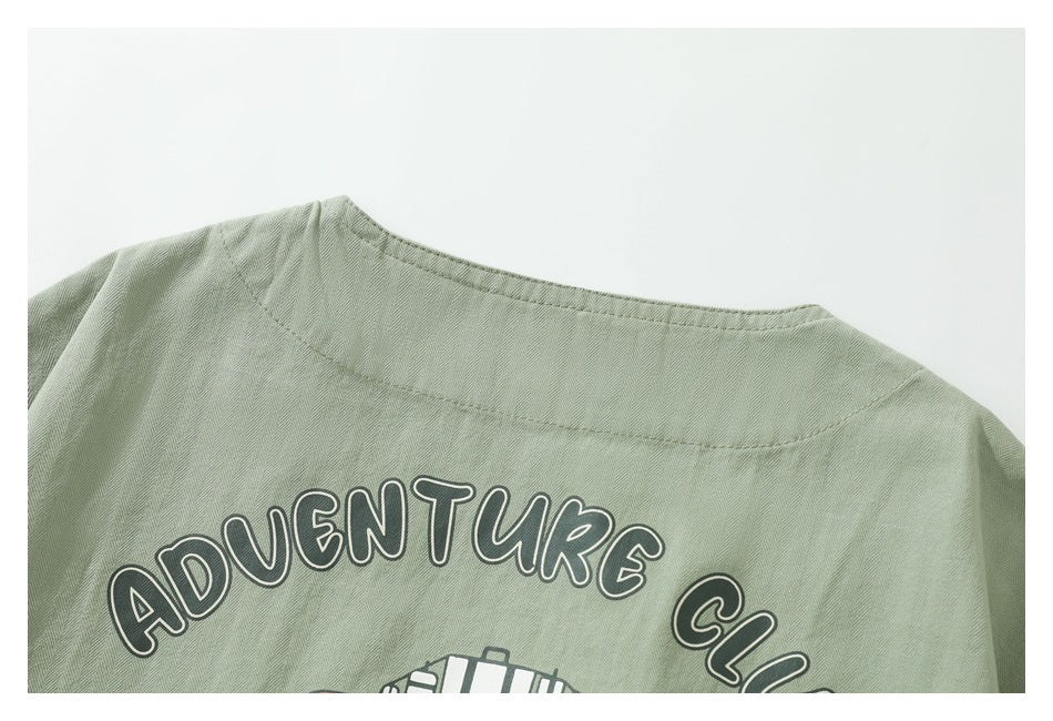 Close-up of a sage green garment’s back with outlined “ADVENTURE CLUB” lettering.
