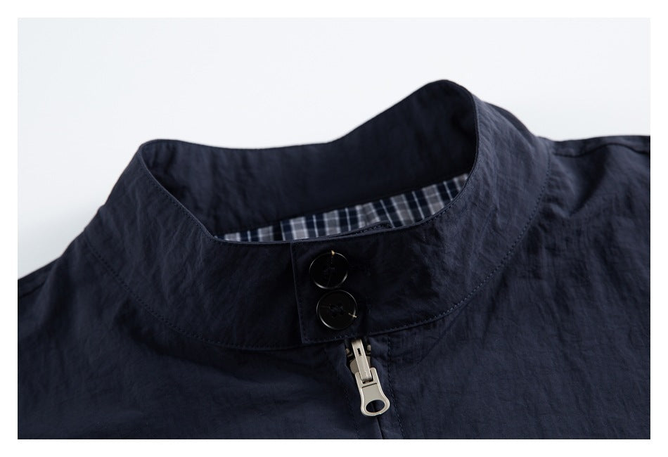 Close-up of a dark navy jacket’s stand collar, two buttons, metal zipper pull and checked inner lining.