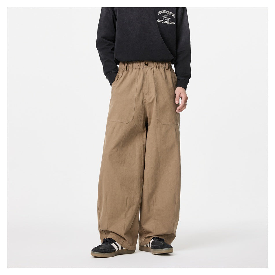 Model wearing loose tan wide-leg trousers with an elastic waistband, button closure and large front patch pockets.