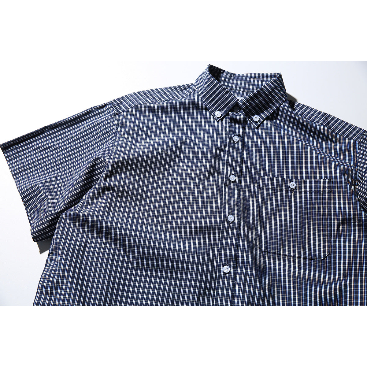 Flat-lay close view of a navy short-sleeve button-up shirt with a white windowpane check and chest pocket.
