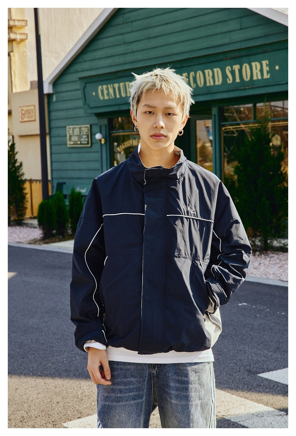 Model wearing a navy jacket with white piping, a high collar, and a concealed front closure.