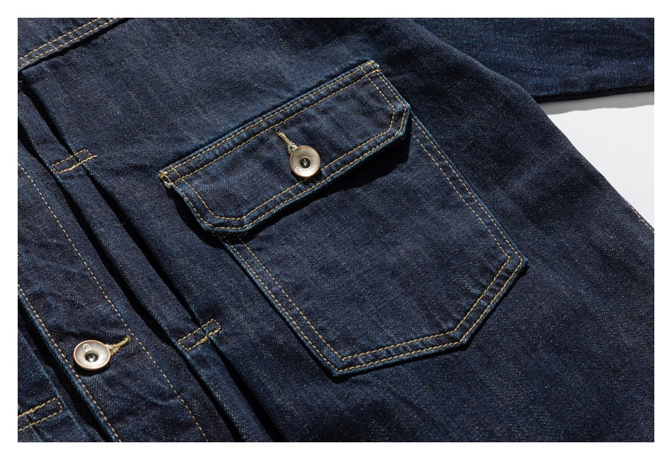 Close-up of a dark indigo denim jacket's buttoned flap pocket and contrast-stitched seams.