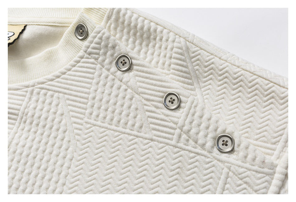 Close-up of four gray buttons on the ivory pullover's shoulder, surrounded by raised geometric stitching.