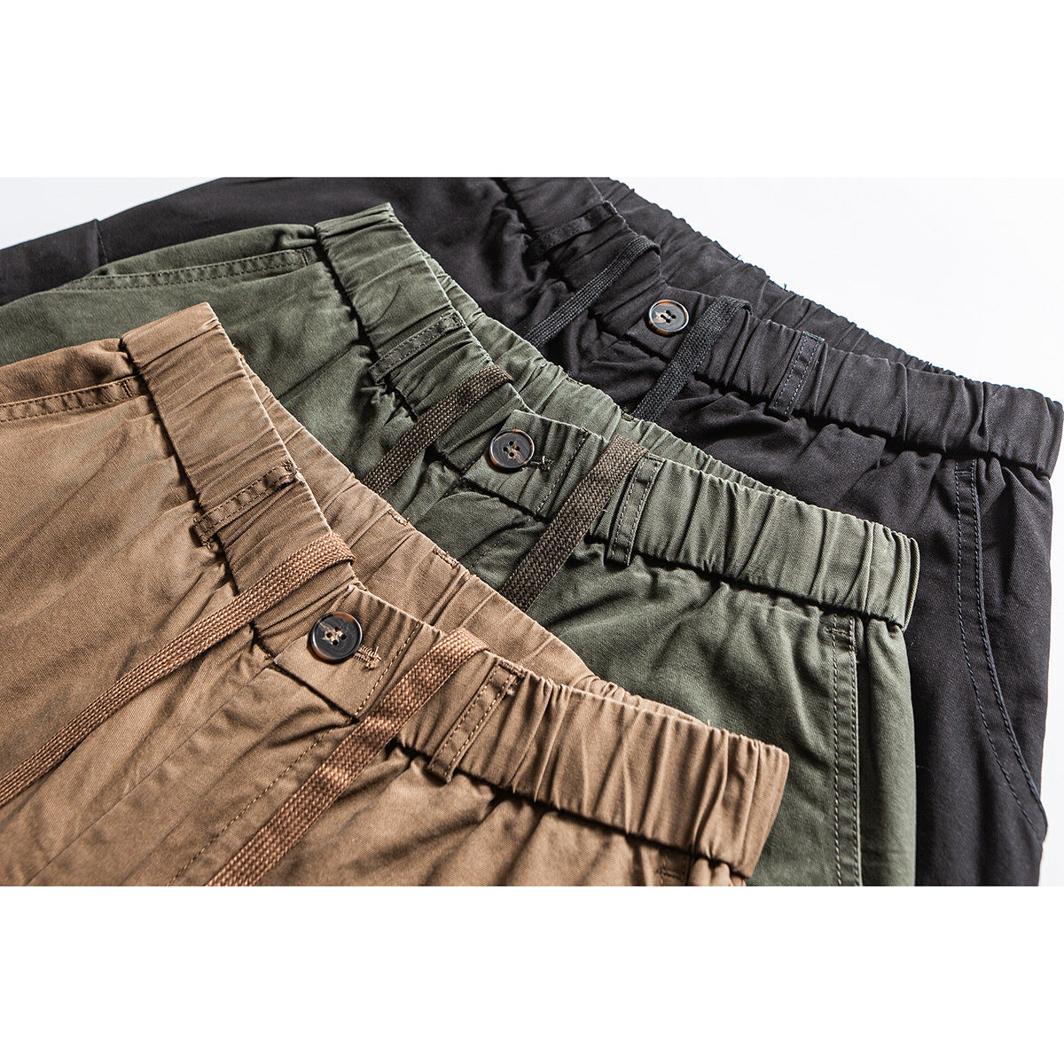 Close-up of elastic waistbands and braided drawcords on black, olive, and brown pants.