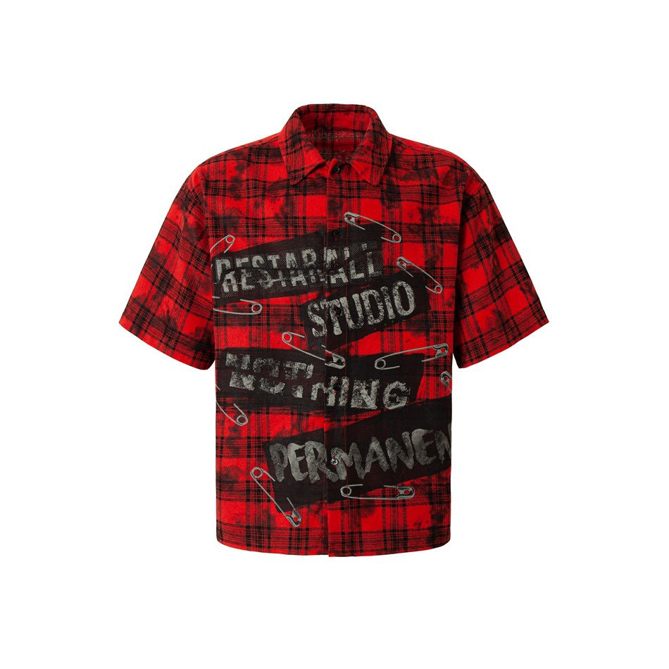 Front view of a red-and-black plaid short-sleeve button-up shirt with a distressed graphic and safety-pin artwork.