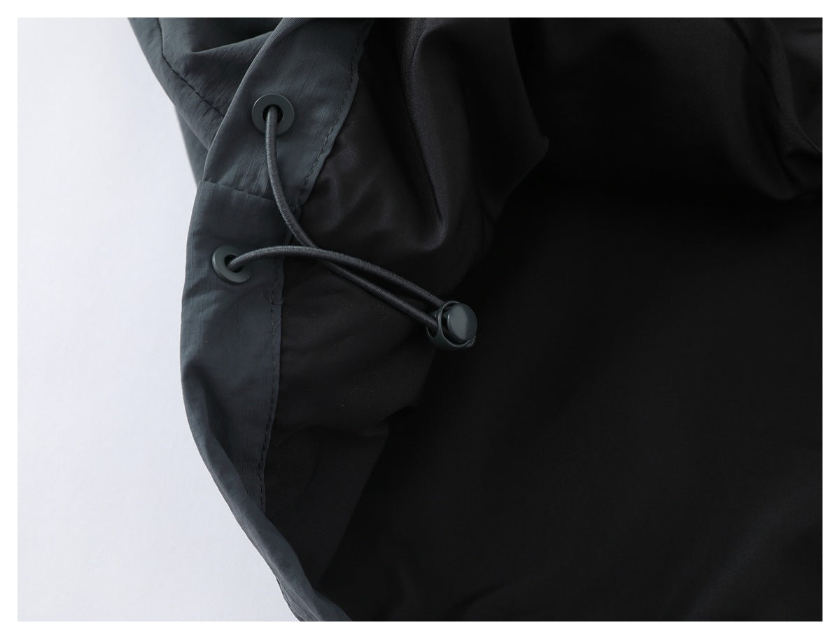 Close-up of a black garment with a dark elastic drawcord, round grommets, and an adjustment toggle.
