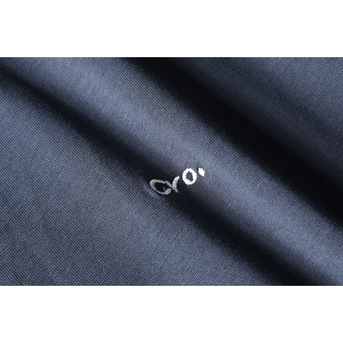 Close-up of a small white embroidered mark on slate-blue knit fabric.