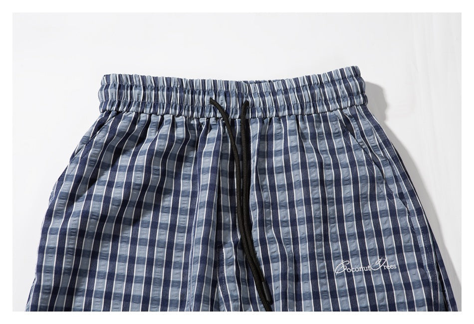 Close-up of the elastic waistband and black drawstring on blue and gray plaid pants, with white embroidered lettering.