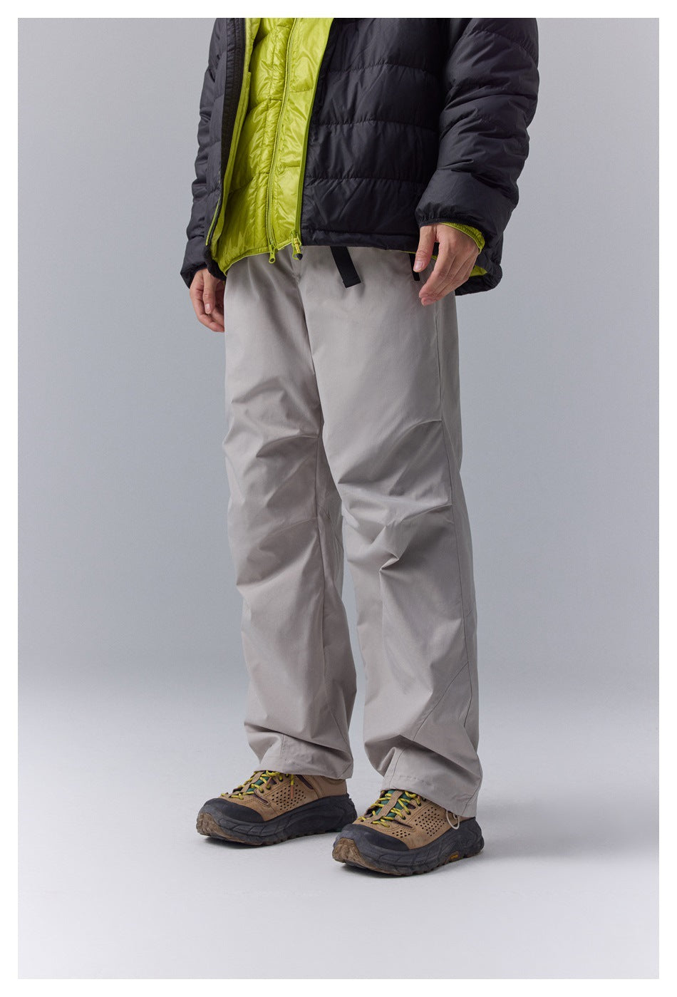 Angled front view of loose-fit light gray pants worn with a black jacket and lime-green inner layer.