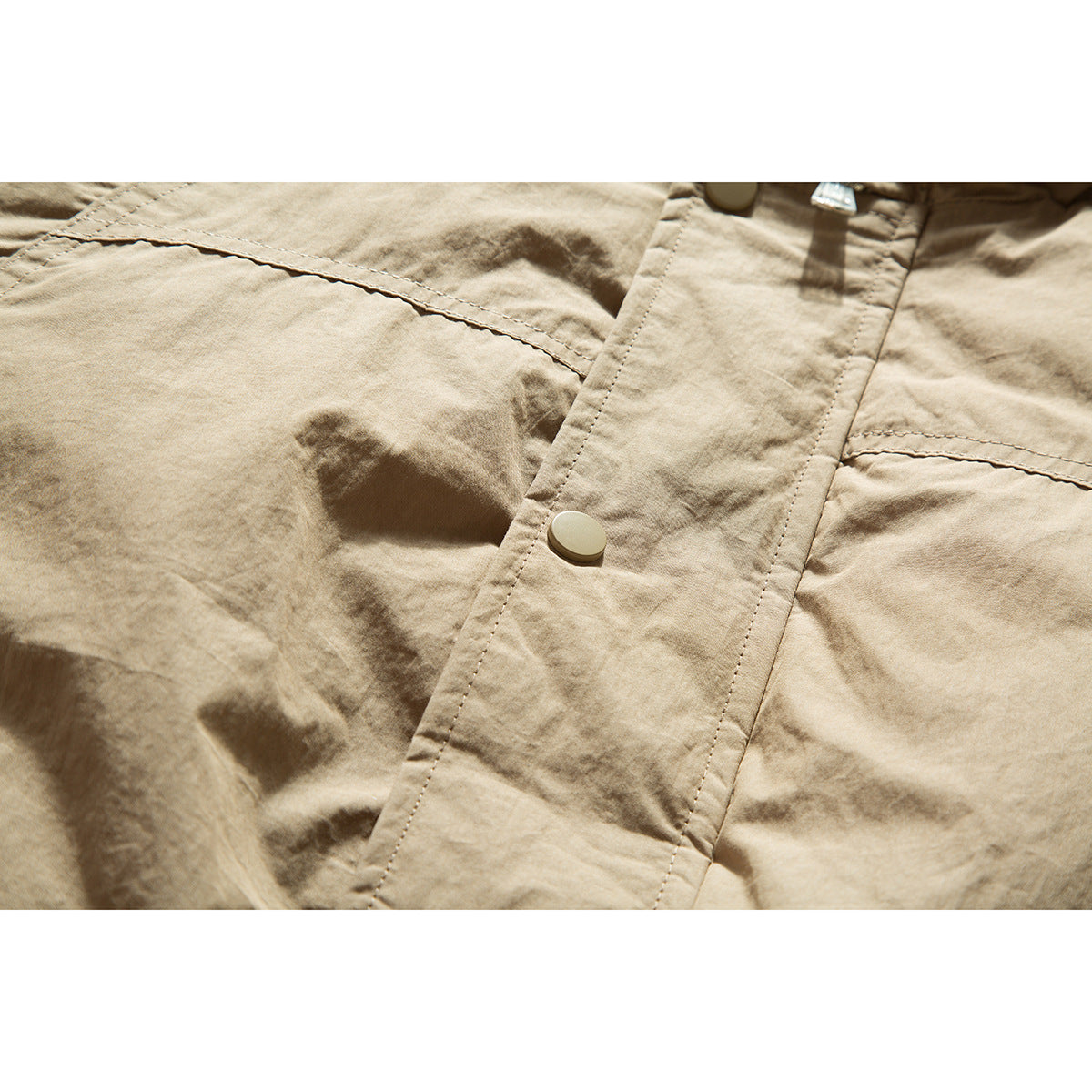 Close-up of tan jacket fabric, a snap-button placket, and stitched panel seams.