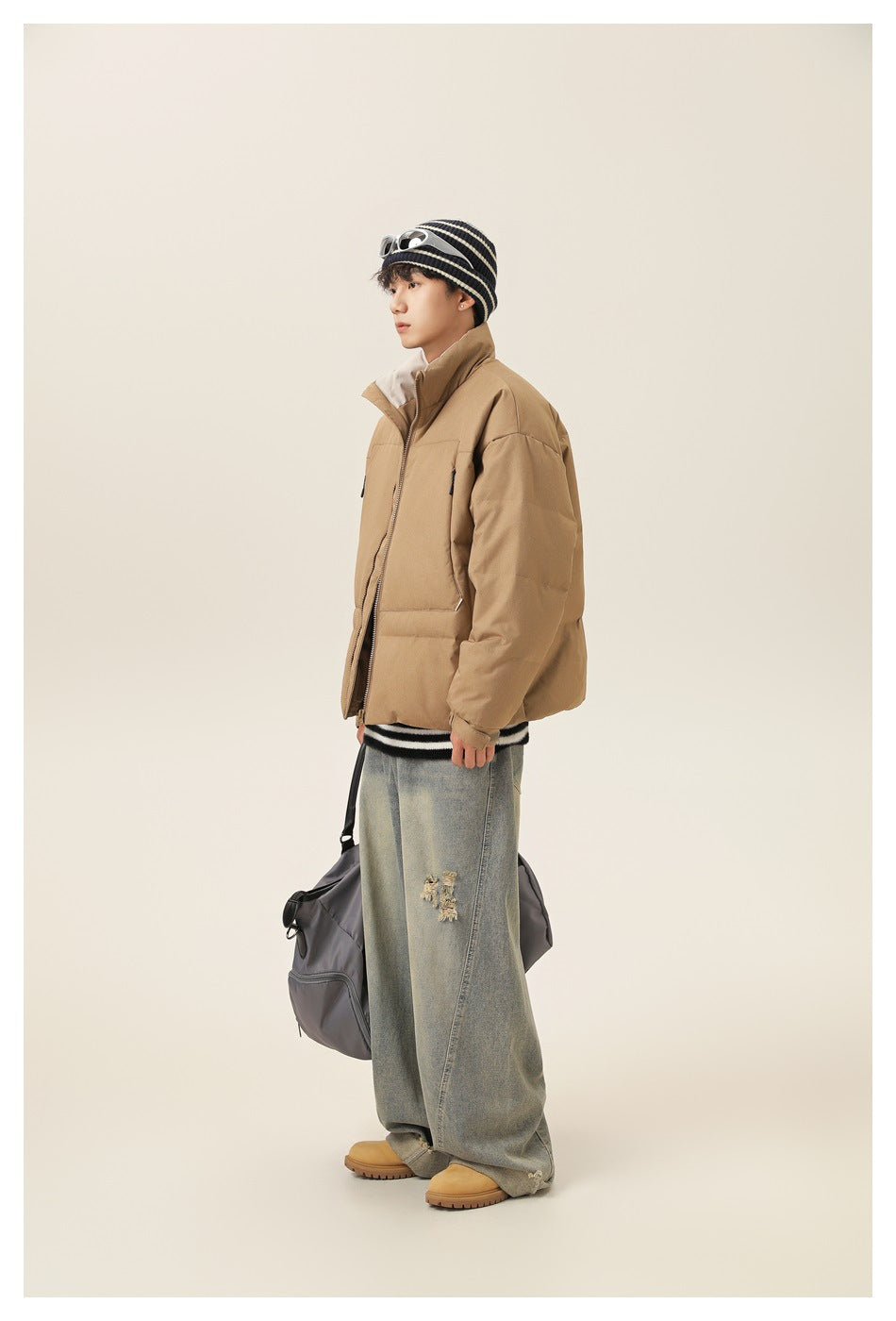 Side view of a model wearing a tan puffer jacket with a high collar, zip front, and roomy pockets.