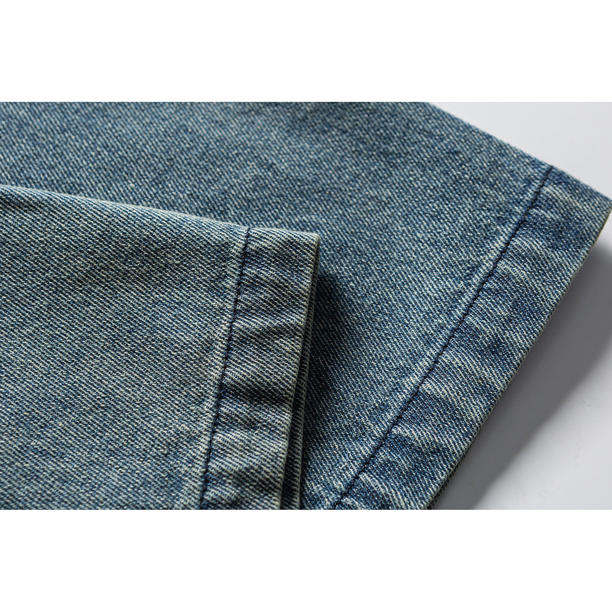 Close-up of washed blue denim fabric with a folded edge and visible stitching.