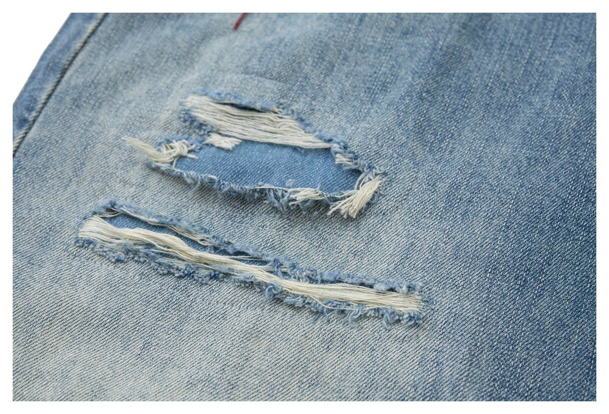 Close-up of light blue jeans with two large frayed tears and exposed white threads.
