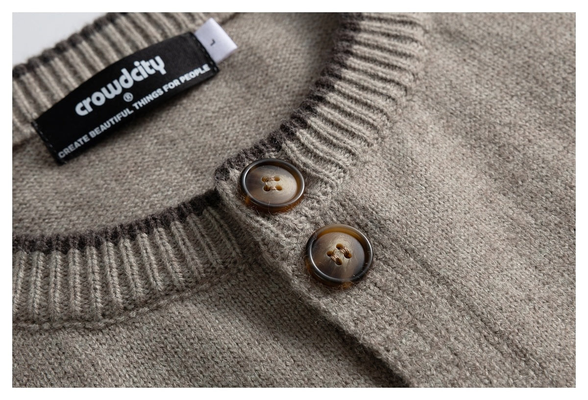 Close-up of a taupe knit cardigan neckline, ribbed trim, two brown buttons, and a black woven label.