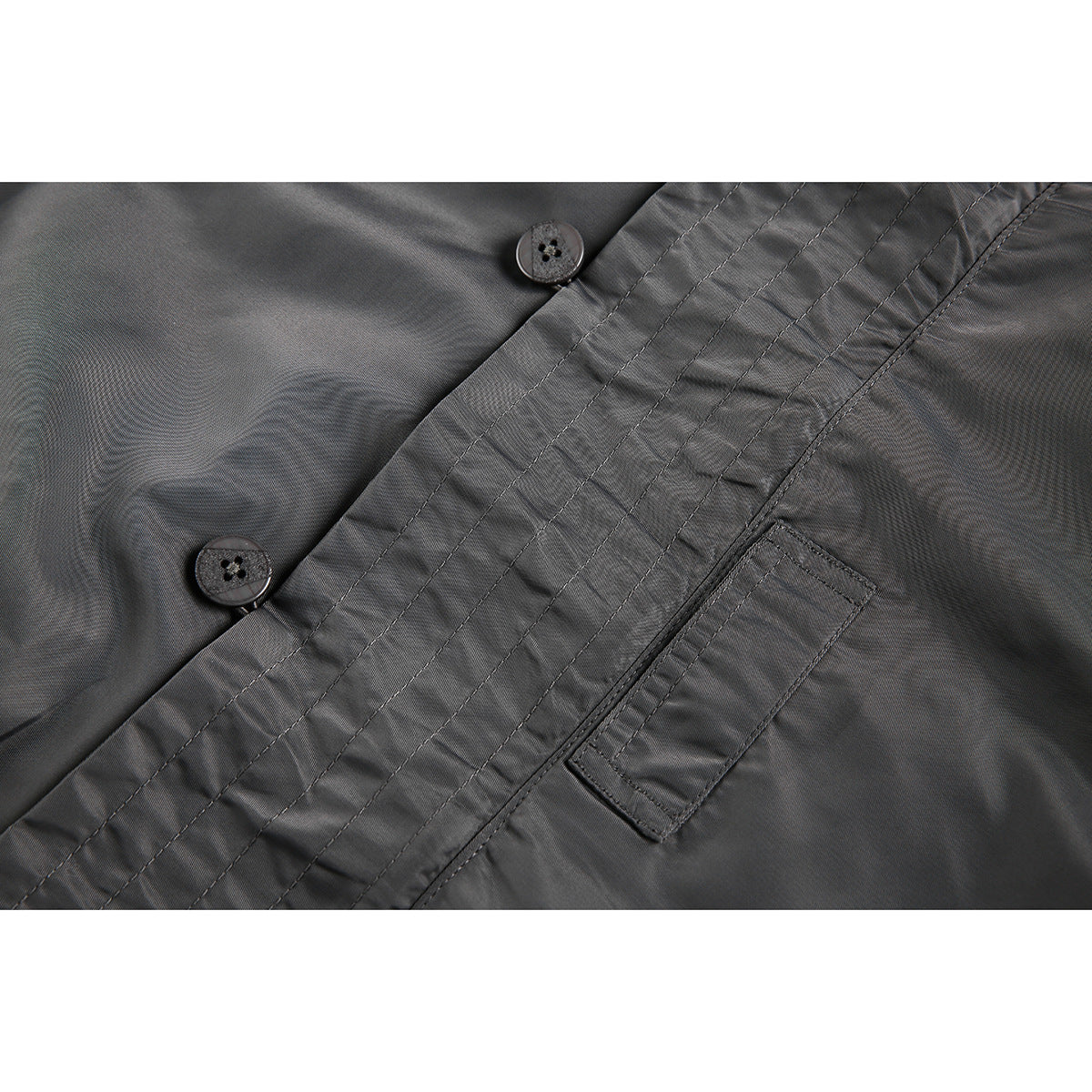 Close-up of a gray jacket's buttoned front placket, parallel stitching, and pocket opening.