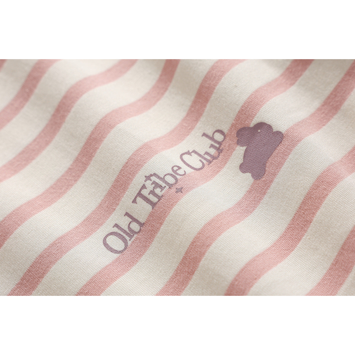 Close-up of cream fabric with dusty pink wavy stripes and a small purple printed wordmark and silhouette.