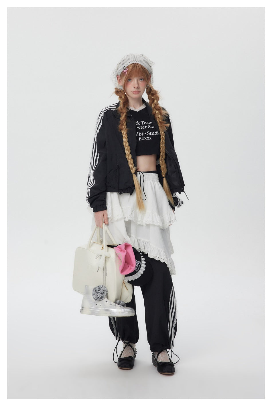 Model in the black cropped jacket with white sleeve stripes and lace, styled with a white tiered skirt and carrying a bag