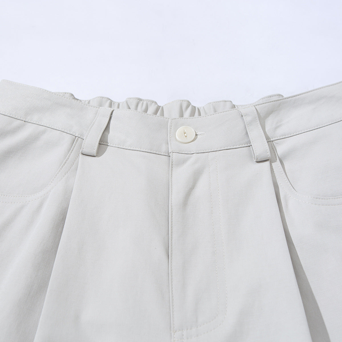 Close-up of ivory wide-leg trousers showing the button closure, belt loops, front pockets and gathered waistband.