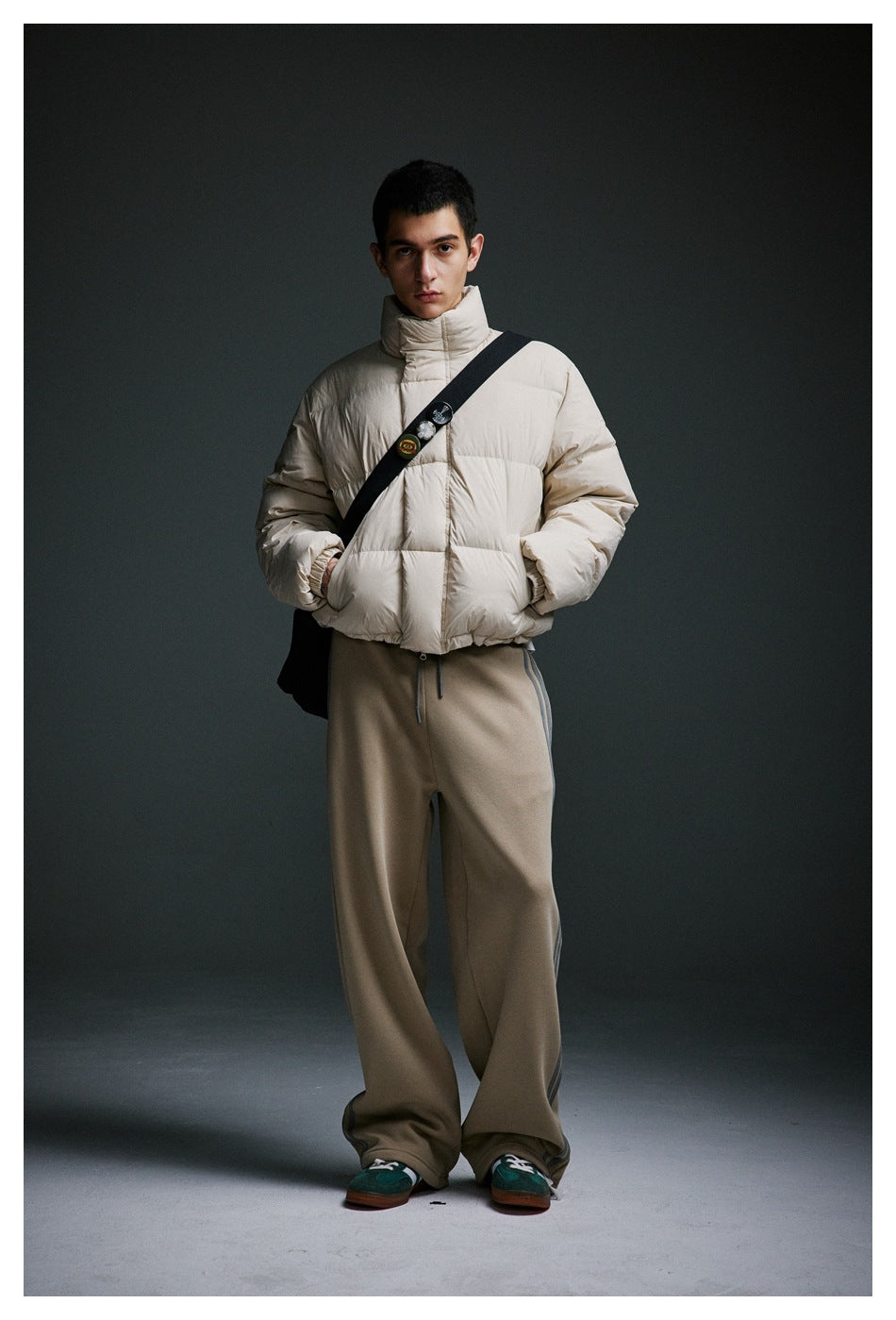 Front view of a model wearing a cream puffer jacket and loose taupe pants with gray side stripes.