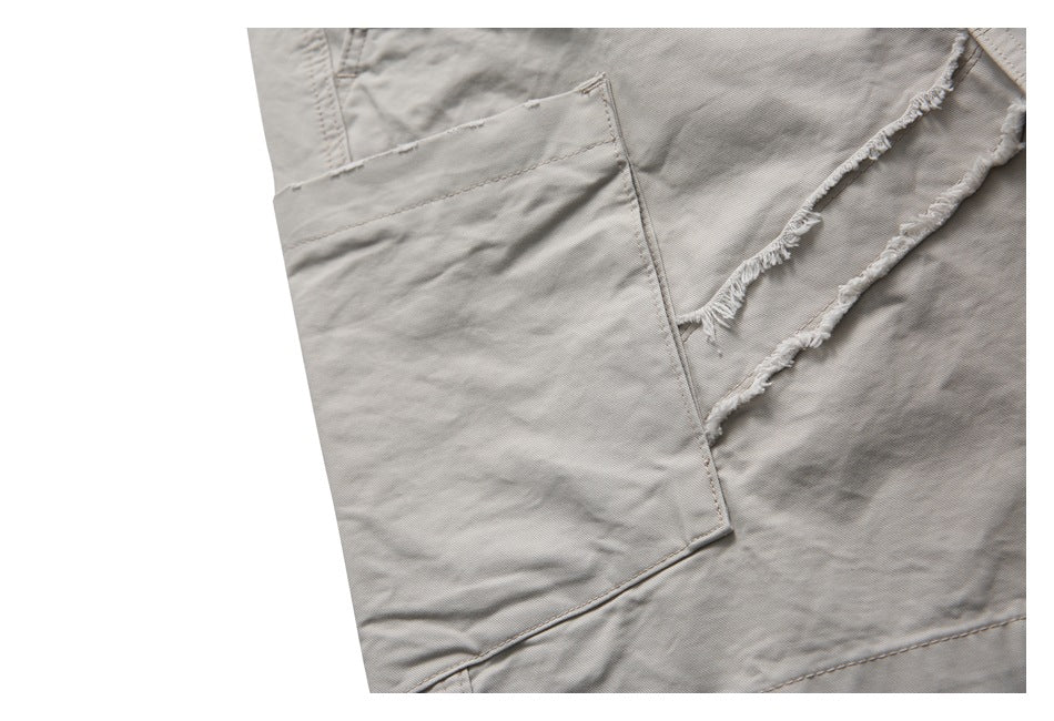 Close-up of light taupe trousers with a large patch pocket beside distressed, frayed seams.