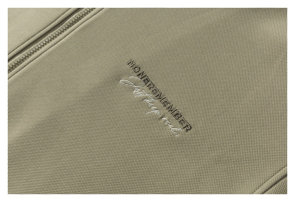 Close-up of olive fabric with embroidered lettering and a diagonal seam.