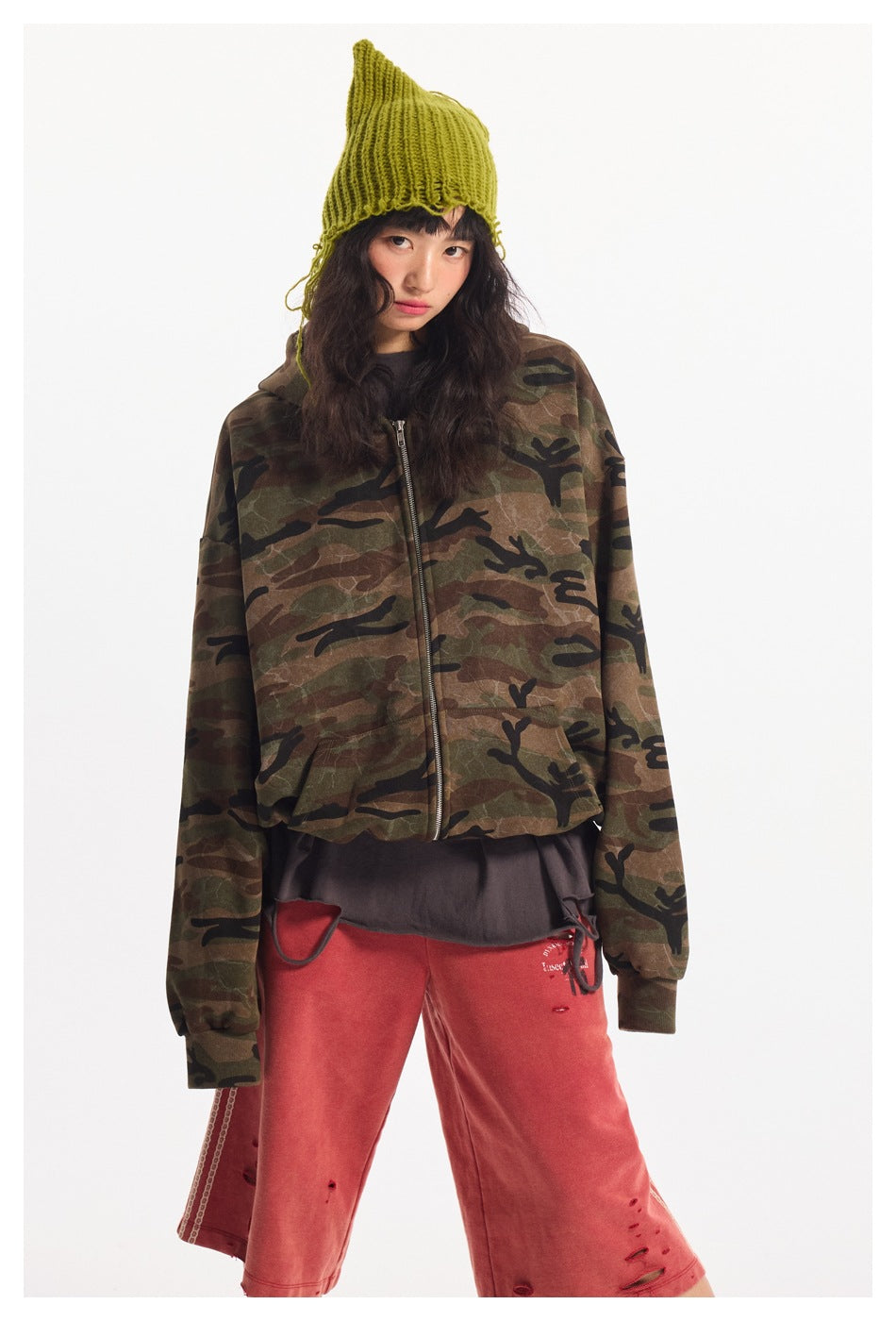 Close-up of a model in a camouflage zip hooded jacket with a green knit beanie and red distressed shorts