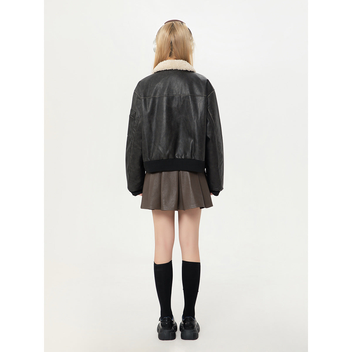 Back view of a model wearing a black jacket with a cream sherpa collar and a brown pleated skirt.