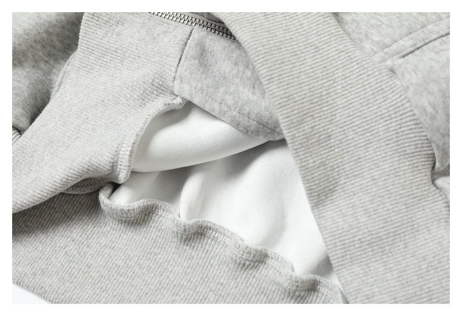 Close-up of light gray ribbed garment trim, stitching, and a section of zipper.