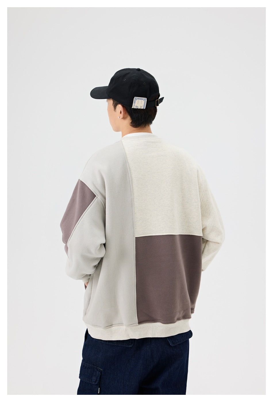 Back view of a person wearing a cream and taupe color-block sweatshirt with dark navy cargo pants and a black cap.
