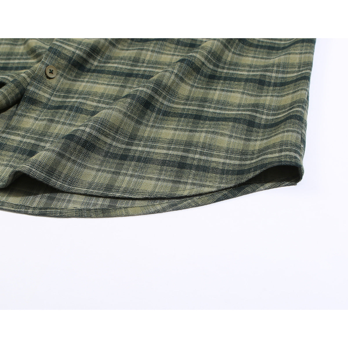 Close-up of the curved hem of an olive and charcoal plaid shirt laid flat.
