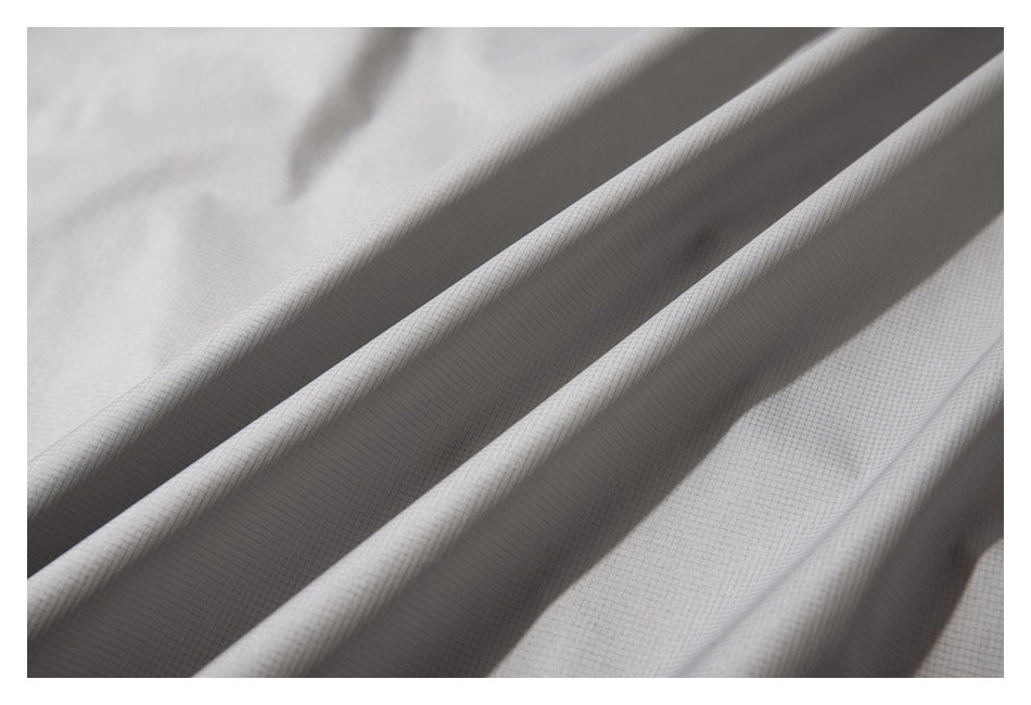 Close-up of light gray fabric showing its fine grid texture and long diagonal folds.