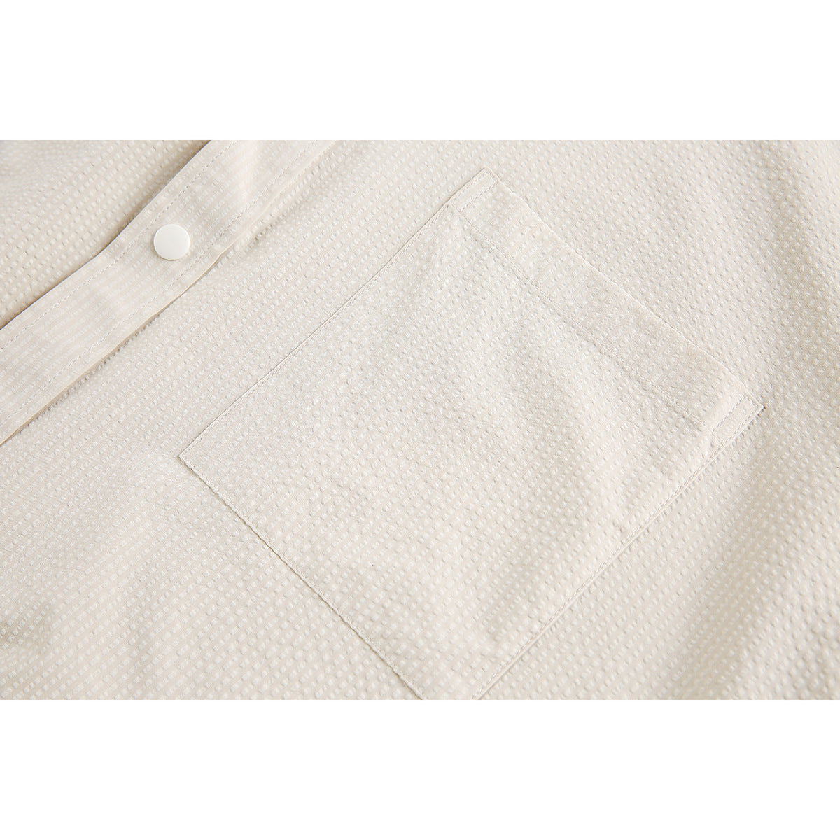 Close-up of a square patch pocket and white snap on cream textured fabric.