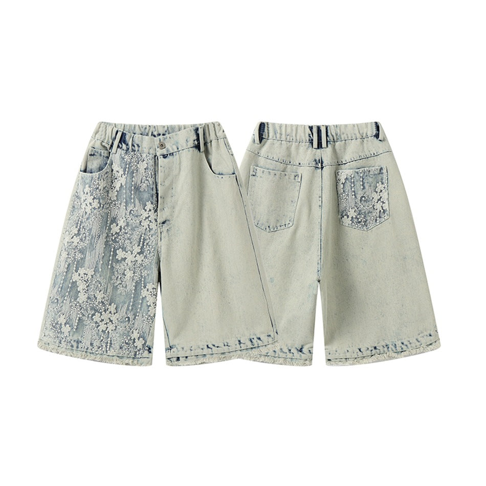 Pale blue acid-wash denim shorts shown from the front and back, with white floral embroidery on one front leg and back