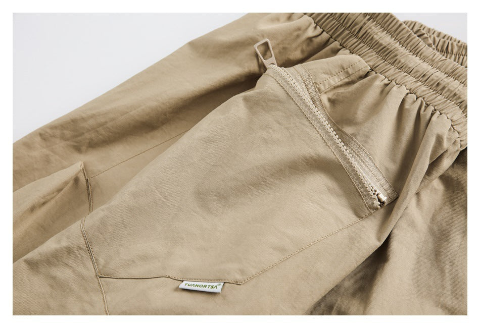 Close-up of tan pants showing an elastic waistband, a zippered pocket, stitching, and a small sewn label.