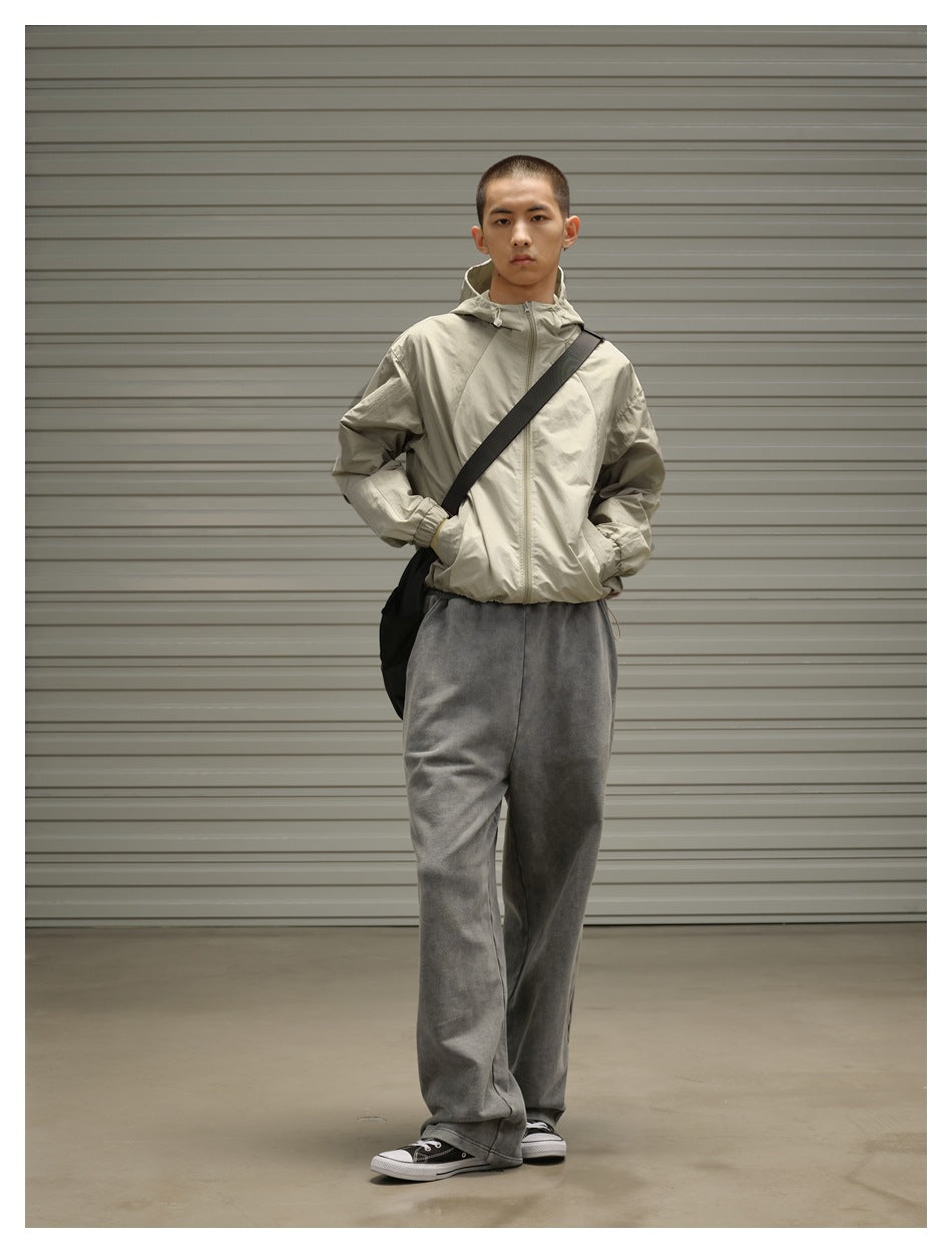Front view of a model wearing a light beige hooded jacket, loose charcoal gray pants, and a black crossbody bag.