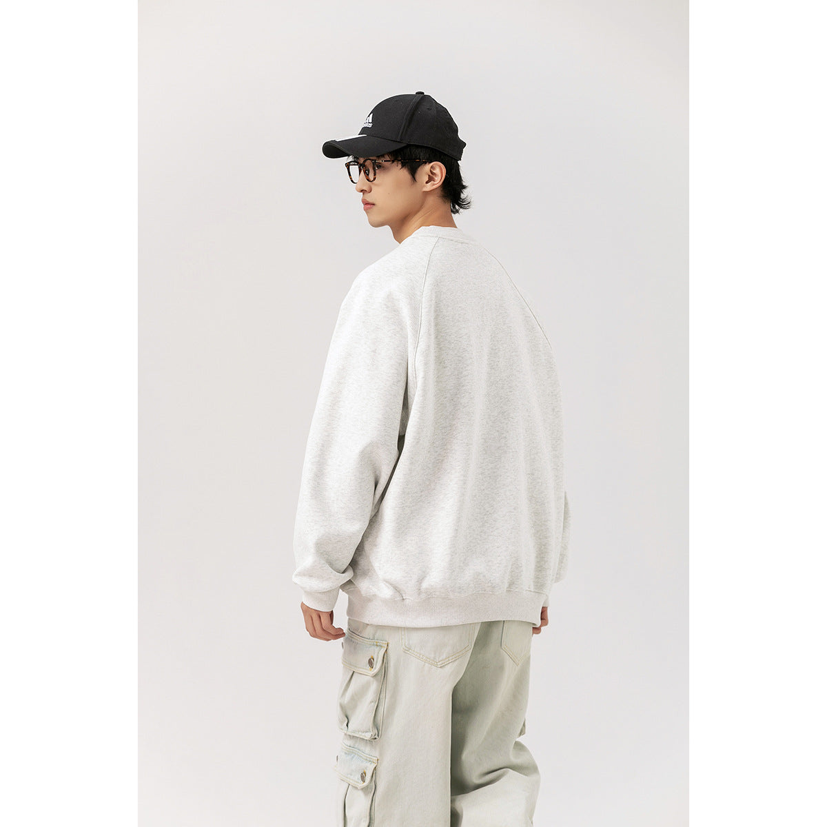 Model wearing a plain light gray sweatshirt, turned to show its back and side.