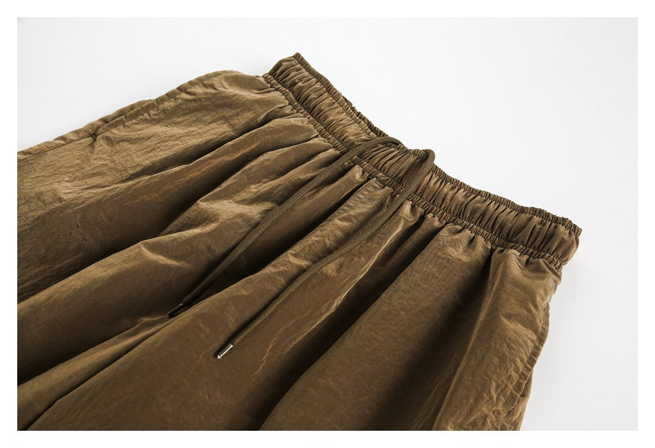 Close view of brown shorts with a gathered elastic waistband, front drawstrings and pleated fabric.
