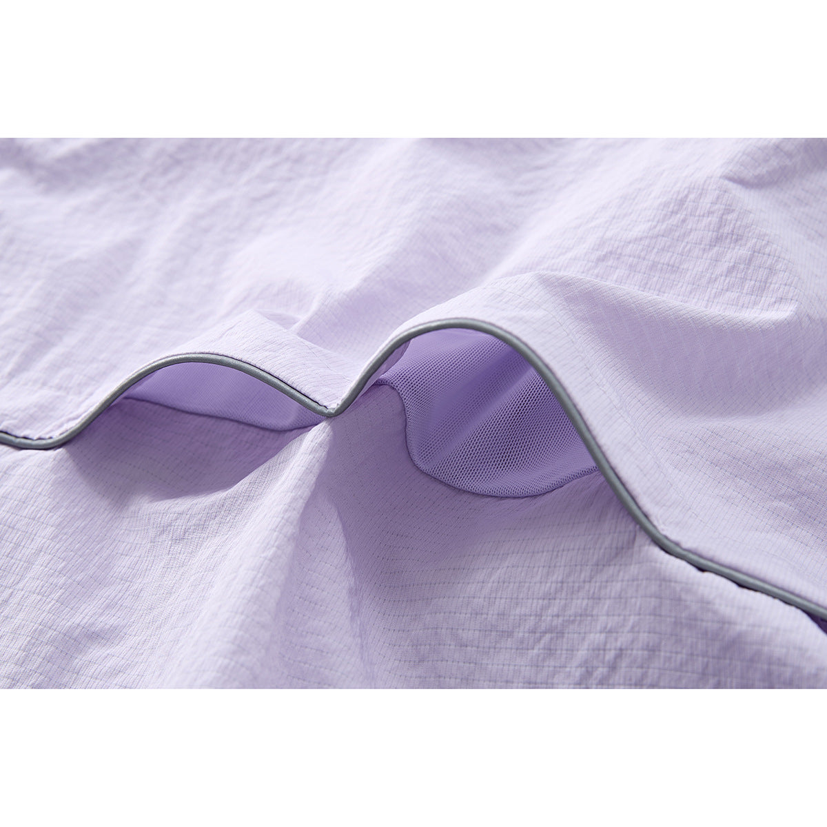 Close-up of pale lavender jacket fabric, showing gray piping and a purple mesh-lined opening.